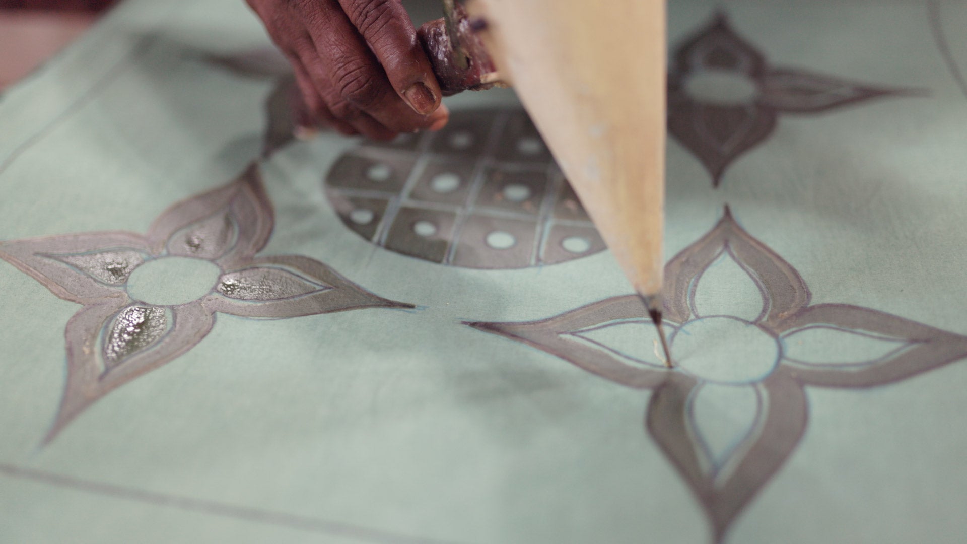 An artisan applies beeswax to fabric using traditional tools in the batik creating process for Kohomba's handcrafted home decor.