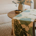 Naari handmade cotton batik table and bed runner in khaki green on rye, 90" x 14", from Kohomba Life – styled on a dining table.